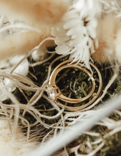 Goldene Eheringe mit Diamant, dekorativ platziert zwischen Blumen und Moos